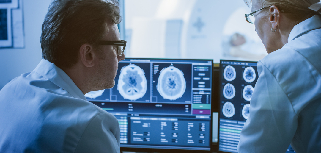 Profissionais de saúde analisando exames de ressonância magnética do cérebro em monitores para diagnóstico por imagem